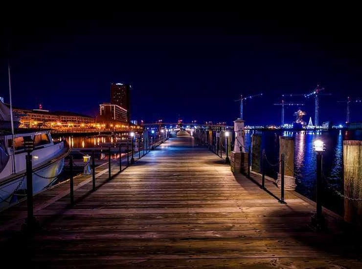Nighttime view of a marina pier with boats and waterfront lights