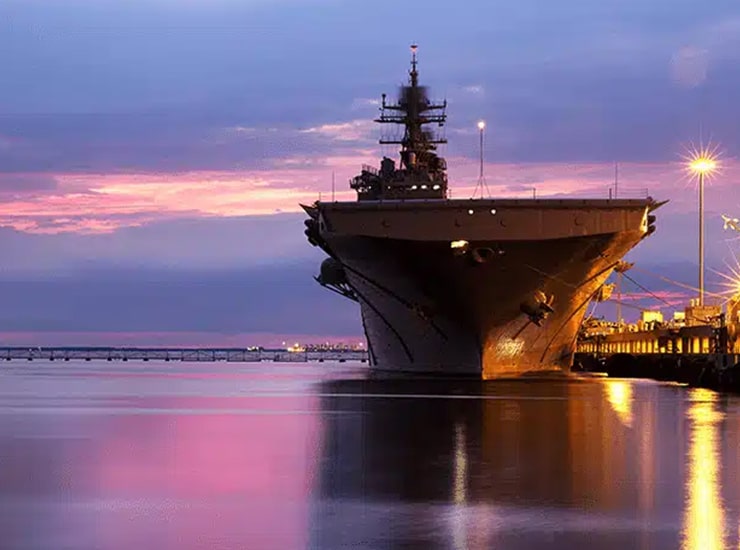 Aircraft carrier docked at a waterfront pier in Hampton Roads at sunset